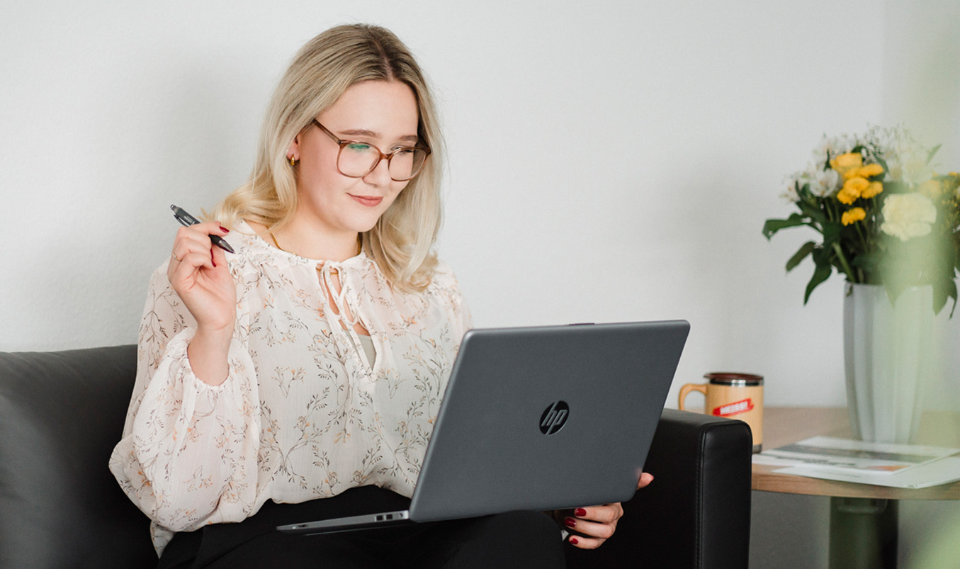 Junge Frau sitzt an Laptop mit Stift in der Hand